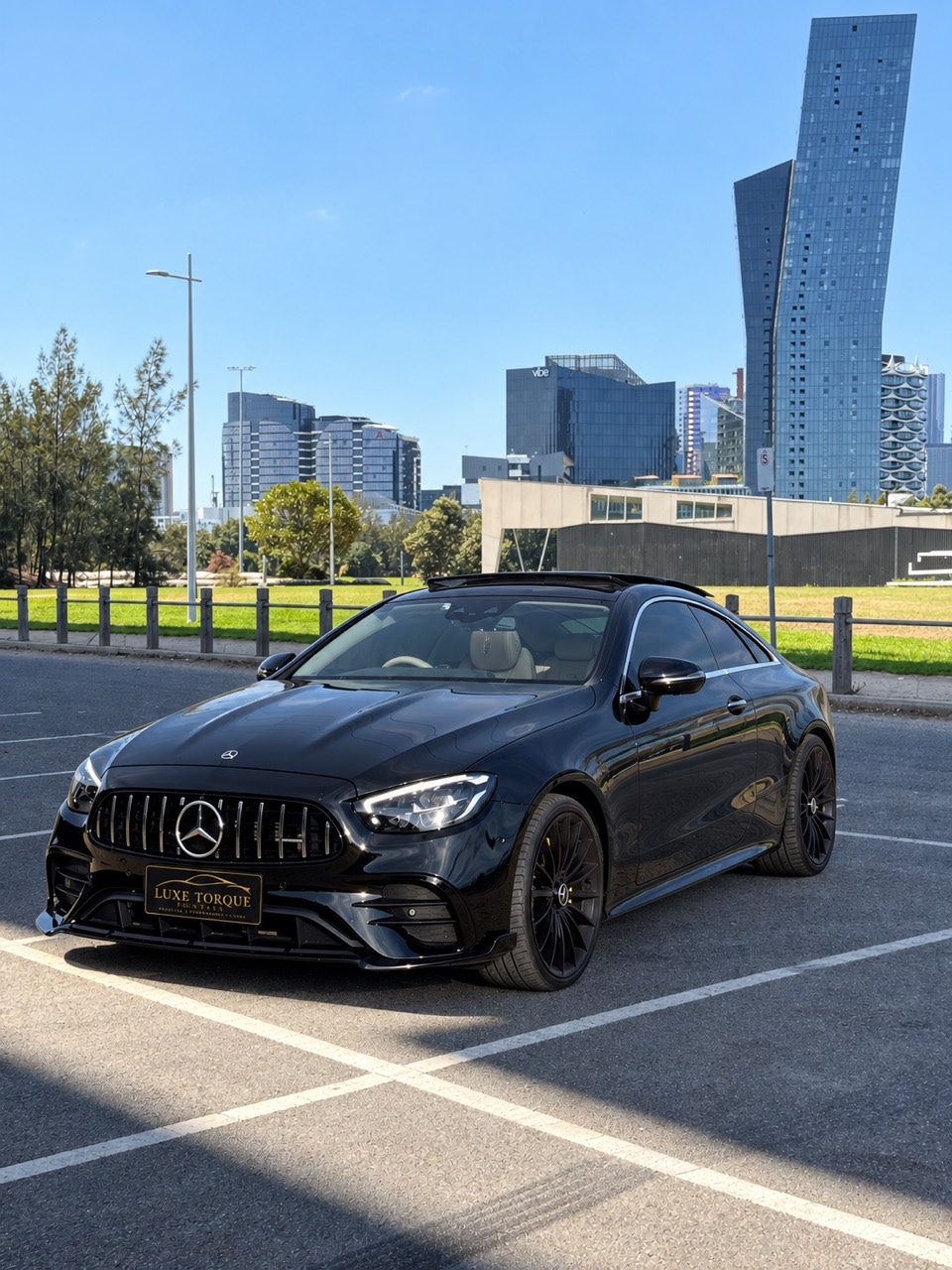 Mercedes-Benz E200 coupe with city background and Luxe Torque Rentals plate